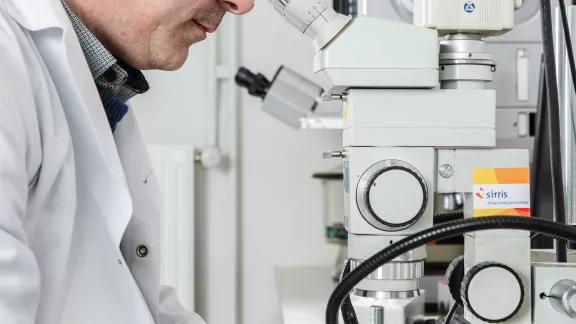 A material expert examines a metal sample through a stereomicroscope fitted with a digital camera for macrographic imaging