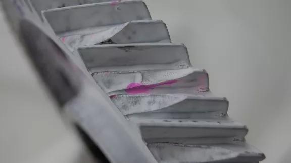 Pink penetrant bleeding through white developer reveals a surface crack on a ribbed metal profile