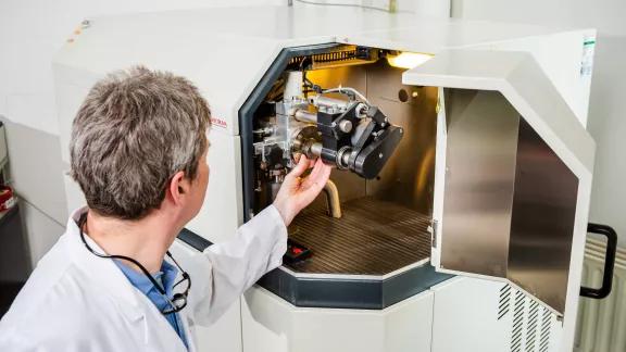 A lab technician positions a metal sample into the sample chamber of a Spectruma GDOES spectrometer