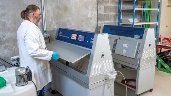 A lab technician uses a handheld radiometer to check UV exposure on panels inside a QUV weathering chamber