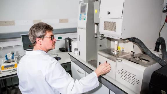 Sirris technician operating a LECO CS230 carbon and sulphur analyser in the metals lab.