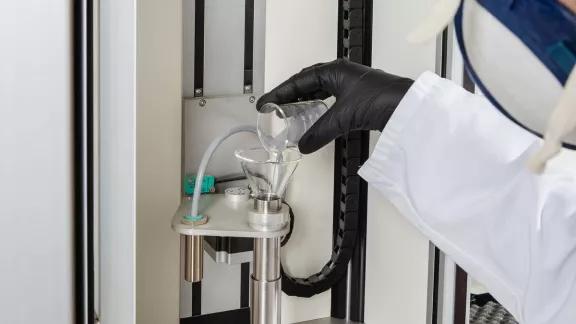 A lab technician pours a powder sample through a funnel into the GranuPack tapping tube