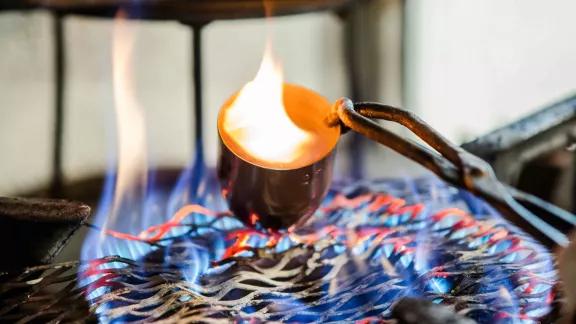 A crucible held with tongs over an open flame during calcination testing to burn away the polymer matrix