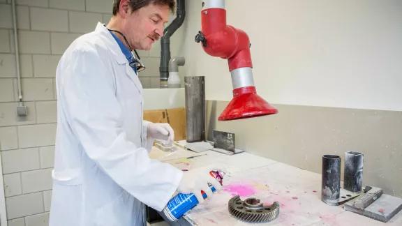 A lab technician sprays red penetrant onto a metal gear as part of a red-white penetrant test