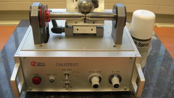 Calotest instrument with a rotating steel ball that grinds a spherical crater through a coating to reveal layer thickness