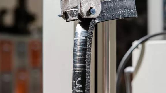 Strip cut from an electrofused polyethylene assembly being peeled apart in the grips of a testing machine
