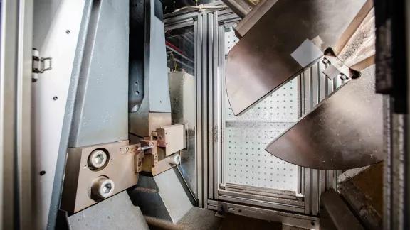 Anvil and specimen support of a Charpy pendulum impact tester with the hammer raised behind a safety enclosure