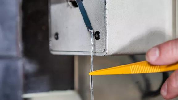 Close-up of a strand of molten polymer emerging from the die of an extrusion plastometer, cut off with tweezers