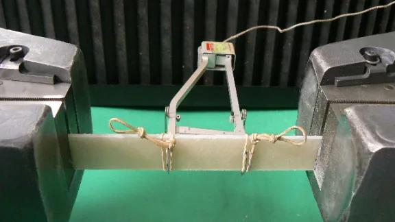 Polyethylene specimen clamped in the grips of a universal testing machine with an extensometer attached