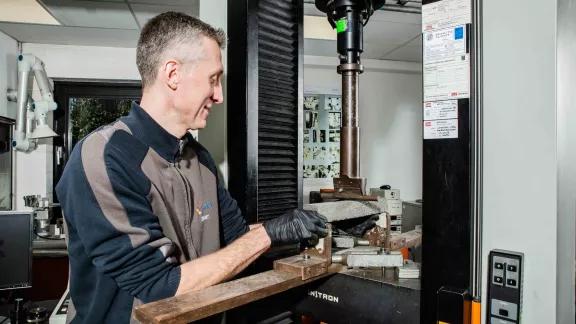 A lab technician smiles while positioning a sample in a three-point bend fixture on an Instron testing machine