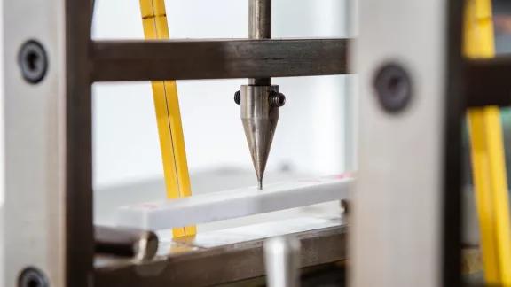 Close-up of a calibrated indenter tip positioned on a plastic sample during Vicat softening point testing