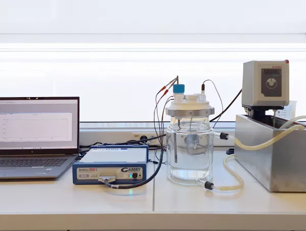 A Gamry Interface 1010E potentiostat connected to a three-electrode electrochemical cell and a temperature-controlled water bath