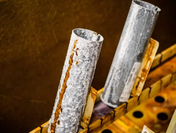 Macro shot of galvanized metal tubes showing rust streaks and pitting after cyclic aging test exposure