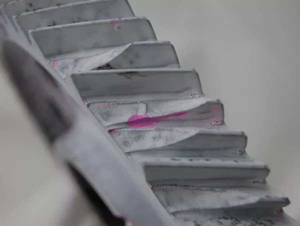 Pink penetrant bleeding through white developer reveals a surface crack on a ribbed metal profile