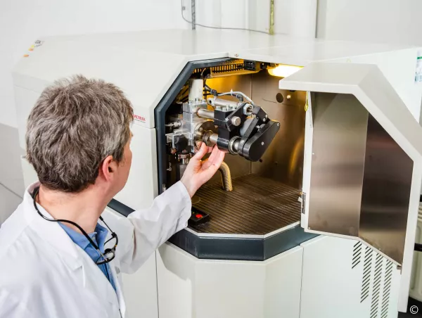 A lab technician positions a metal sample into the sample chamber of a Spectruma GDOES spectrometer