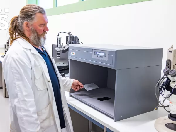 A lab technician places a metal test panel into a Verivide light box used for color measurement