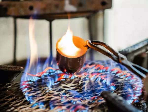 A crucible held with tongs over an open flame during calcination testing to burn away the polymer matrix