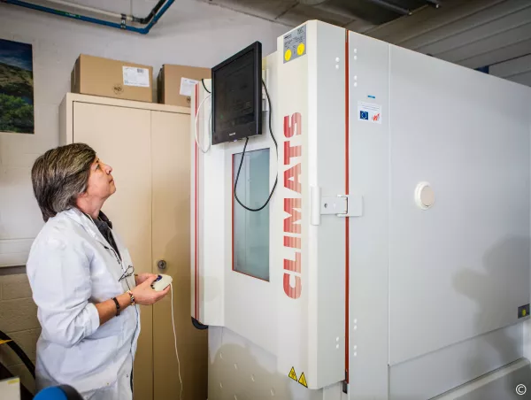 A lab technician in a white coat operates the control panel of a Climats climate test cabinet in the Sirris Liège laboratory