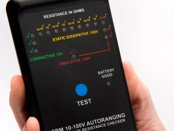Hand holding a surface resistance checker with an indicator scale ranging from conductive to insulative