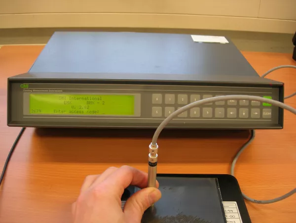 Operator positioning a handheld probe on a coated panel, connected to a coating thickness measurement unit