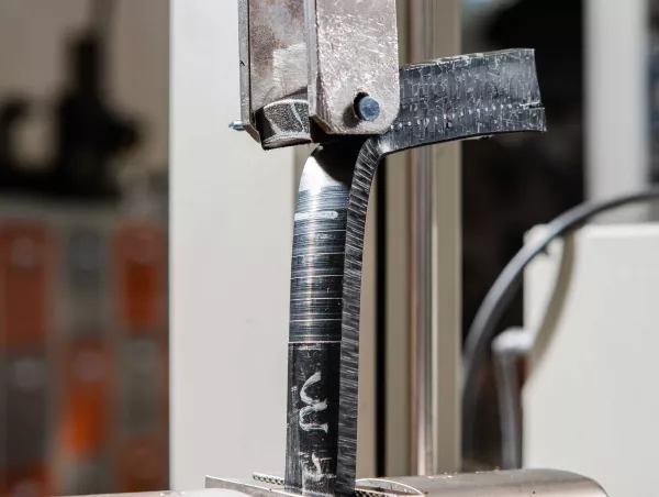 Strip cut from an electrofused polyethylene assembly being peeled apart in the grips of a testing machine