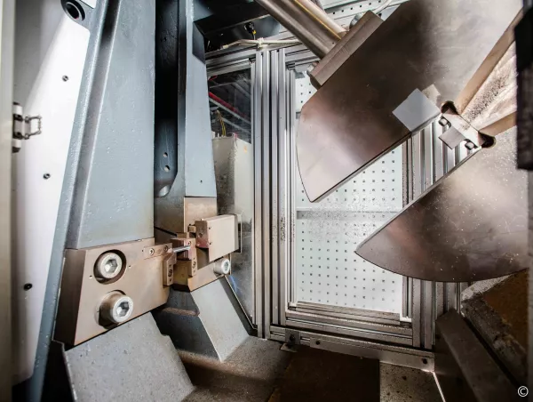 Anvil and specimen support of a Charpy pendulum impact tester with the hammer raised behind a safety enclosure