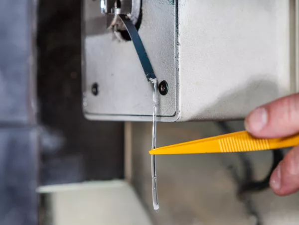 Close-up of a strand of molten polymer emerging from the die of an extrusion plastometer, cut off with tweezers