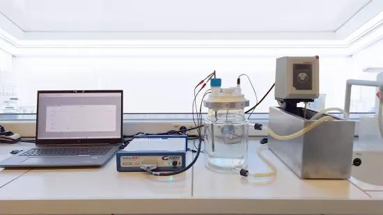 A Gamry Interface 1010E potentiostat connected to a three-electrode electrochemical cell and a temperature-controlled water bath