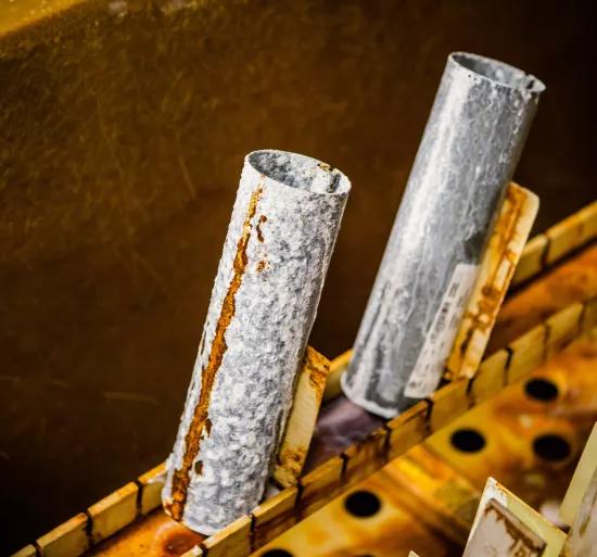 Macro shot of galvanized metal tubes showing rust streaks and pitting after cyclic aging test exposure