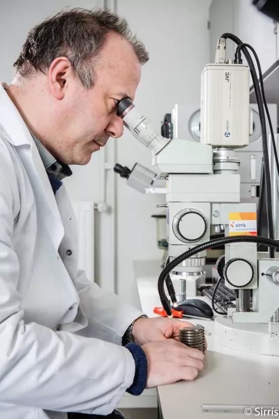 A material expert examines a metal sample through a stereomicroscope fitted with a digital camera for macrographic imaging