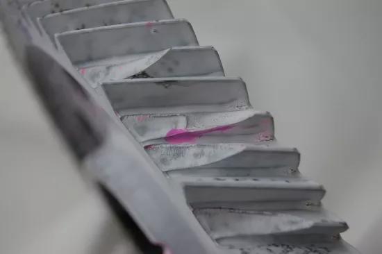 Pink penetrant bleeding through white developer reveals a surface crack on a ribbed metal profile