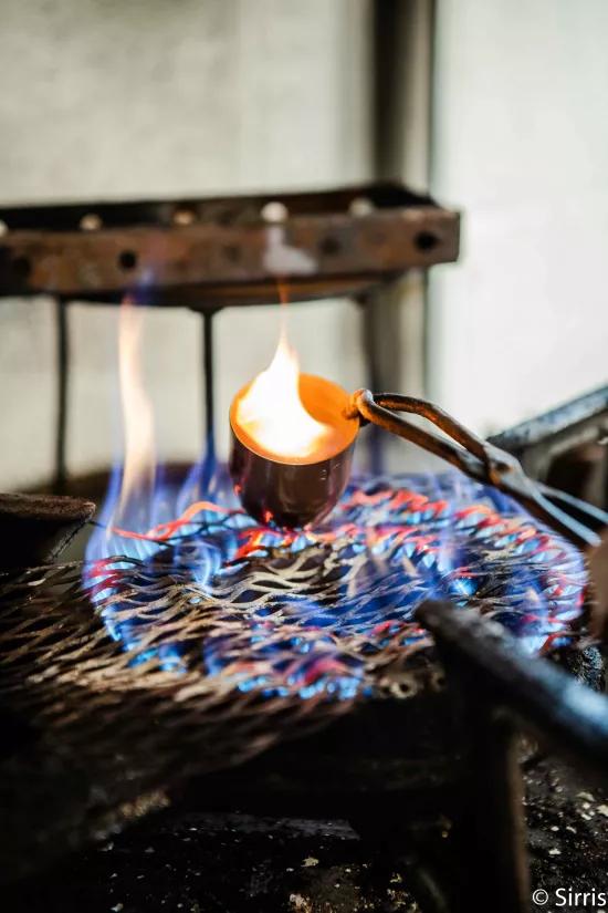 A crucible held with tongs over an open flame during calcination testing to burn away the polymer matrix