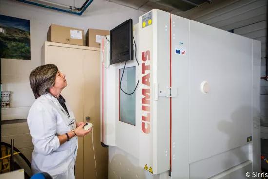 A lab technician in a white coat operates the control panel of a Climats climate test cabinet in the Sirris Liège laboratory