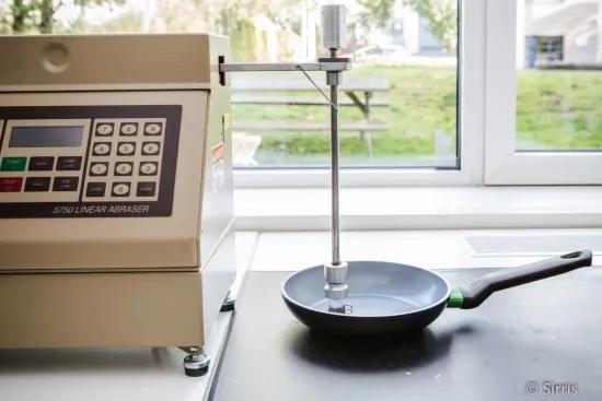 A Taber 5750 Linear Abraser positioned above a black frying pan for a linear abrasion durability test