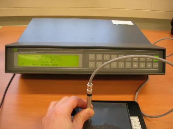 Operator positioning a handheld probe on a coated panel, connected to a coating thickness measurement unit