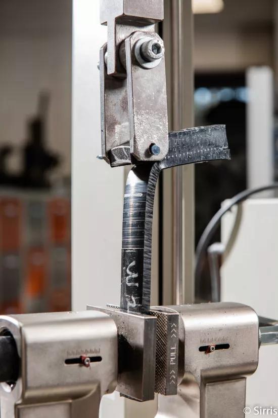 Strip cut from an electrofused polyethylene assembly being peeled apart in the grips of a testing machine