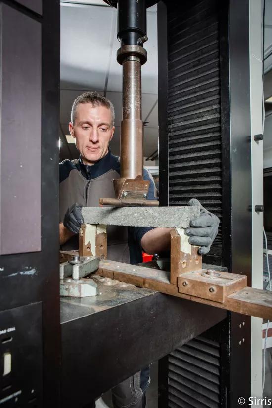 A lab technician positions a composite sample in a three-point bending fixture on an Instron testing machine